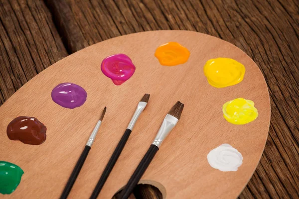 Tavolozza di legno con più colori e pennelli — Foto Stock