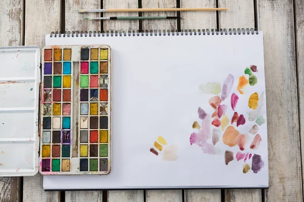 Colorful palette, paintbrushes and paper on wooden surface — Stock Photo, Image