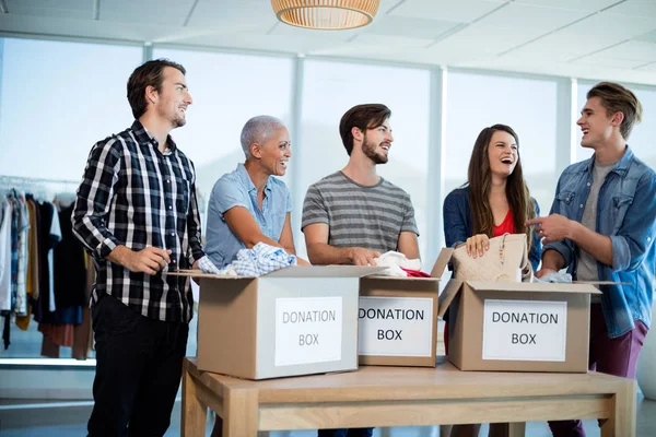 Счастливая команда креативного бизнеса сортирует одежду в коробке для пожертвований — стоковое фото