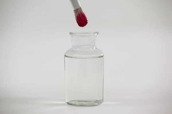 Štětec s růžovou barvou ponoří do sklenice naplněné vodou — Stock fotografie