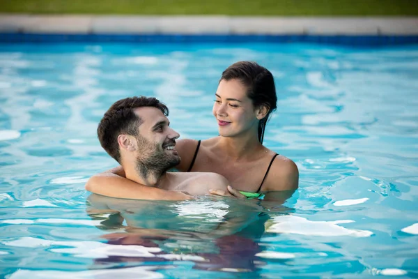 Jong koppel elkaar omarmen in het zwembad — Stockfoto