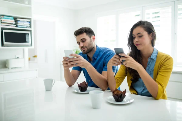 Casal usando telefone celular na cozinha — Fotografia de Stock