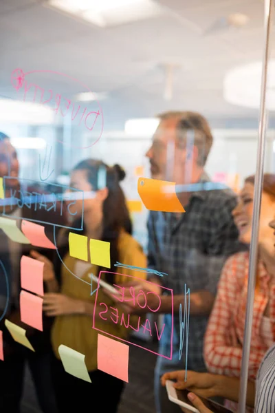 Creative business team looking at sticky notes on glass window — Stock Photo, Image