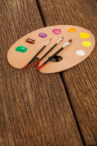 Wooden palette with multiple colors and paint brushes — Stock Photo, Image