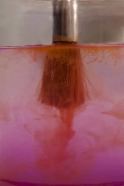 Кисть с розовой краской, погруженной в банку, наполненную водой — стоковое фото