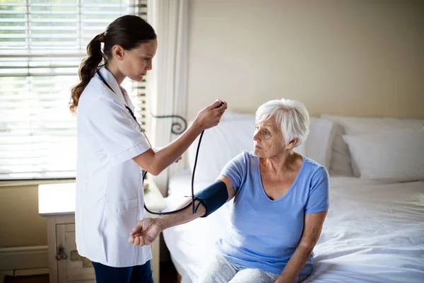 Vrouwelijke arts controle van de bloeddruk van senior vrouw in de slaapkamer — Stockfoto