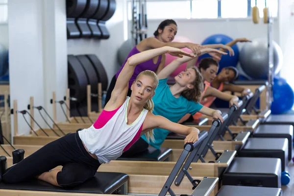 Female trainer assisting group of women with stretching exercise on reformer — Stock Photo, Image