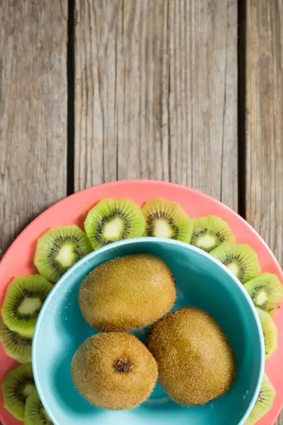Kiwis arranged in bowl and plate on wooden table — Stock Photo, Image