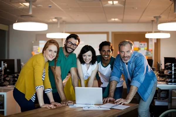 Sorrindo equipe de negócios criativa apoiando-se na mesa e usando laptop no escritório — Fotografia de Stock