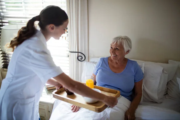 Vrouwelijke arts serveert ontbijt aan senior vrouw in de slaapkamer — Stockfoto