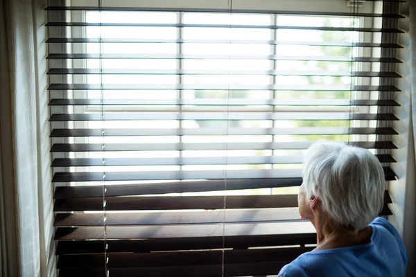 年配の女性が窓のブラインドから外を見て — ストック写真