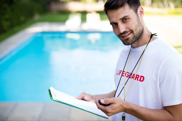 Portrait of lifeguard holding clipboard and stopwatch at poolside — Stock Photo, Image