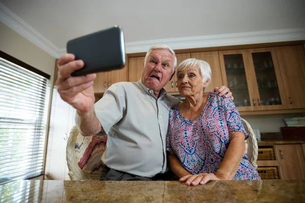 Старшая женщина делает селфи с мобильного телефона на кухне — стоковое фото