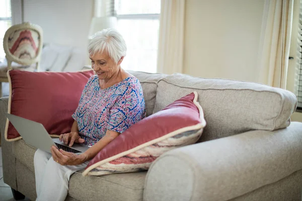 Senior kvinna använder laptop i vardagsrum — Stockfoto