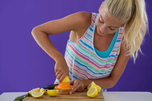 Woman preparing lemon juice from juicer against violet background — Stock Photo, Image