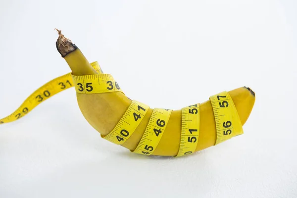 Close-up of fresh banana wrapped with measuring tape — Stock Photo, Image