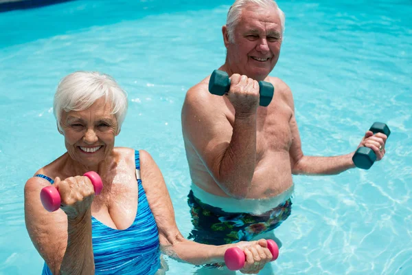 Casal sênior se exercitando com halteres na piscina — Fotografia de Stock