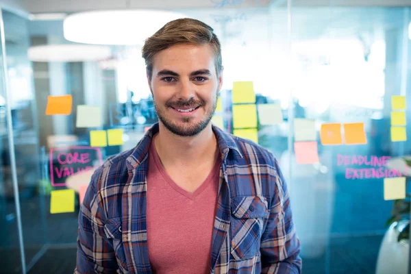 Sorrindo homem de pé contra notas pegajosas na parede de vidro no escritório — Fotografia de Stock