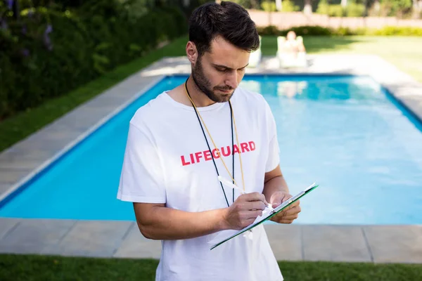 Lifeguard writing on clipboard at poolside — Stock Photo, Image
