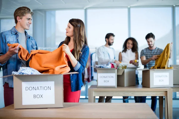 Creatieve business team sorteren van kleding in donatie box — Stockfoto