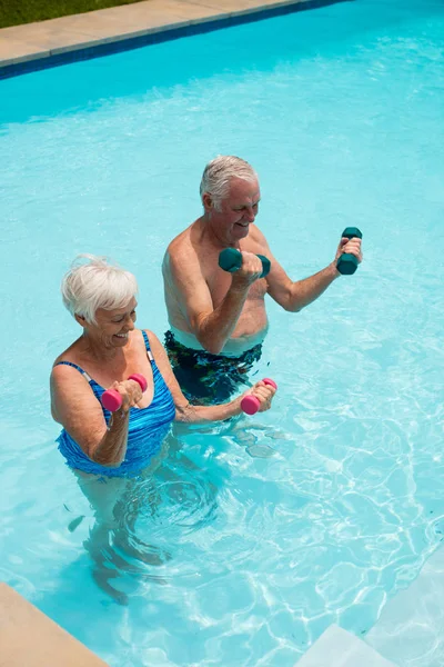 Casal sênior se exercitando com halteres na piscina — Fotografia de Stock