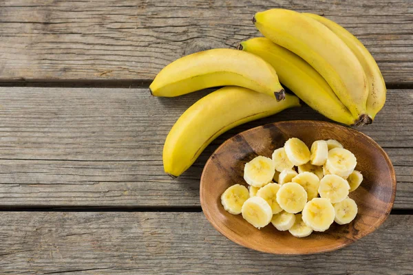 Банан і скибочки банана в тарілці на дерев'яному столі — стокове фото