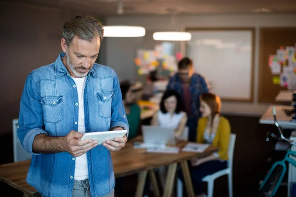 Mann nutzt digitales Tablet, während Team im Hintergrund arbeitet — Stockfoto