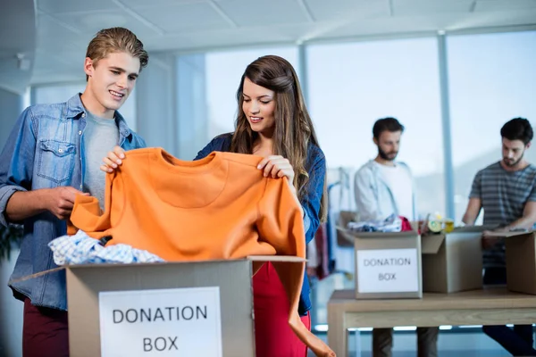 Equipe de negócios criativa classificando roupas em caixa de doação — Fotografia de Stock