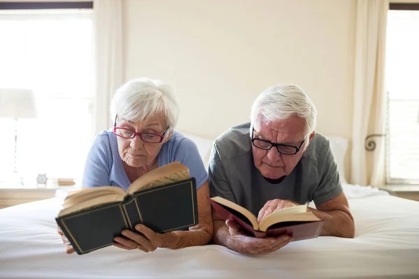 Старшая пара читает книги на кровати — стоковое фото