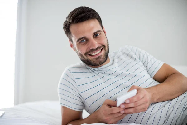 Portret mężczyzny przy użyciu telefonu komórkowego na łóżku — Zdjęcie stockowe