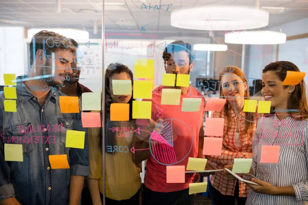 Creative business team looking at sticky notes on glass window in office — Stock Photo, Image