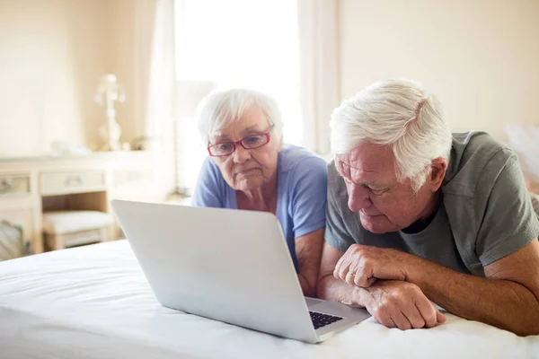 Äldre par med laptop på sängen i sovrummet — Stockfoto