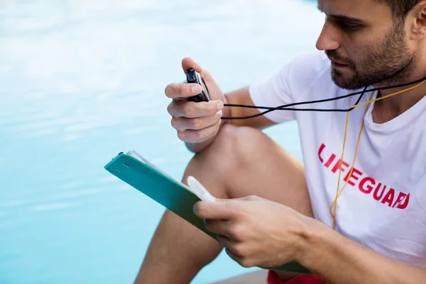 Lifeguard holding clipboard and stopwatch at poolside — Stock Photo, Image