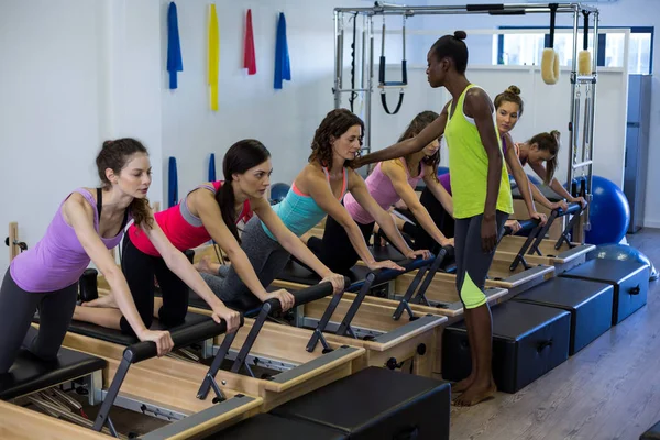 Vrouwelijke trainer bijstaan groep vrouwen met stretching oefening op hervormer — Stockfoto