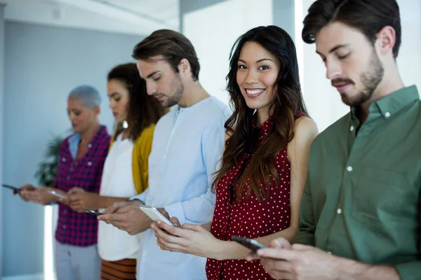 Donna sorridente utilizzando il telefono cellulare con i loro colleghi in ufficio — Foto Stock