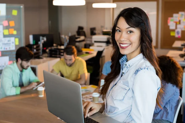 Усміхнена жінка використовує ноутбук в офісі — стокове фото