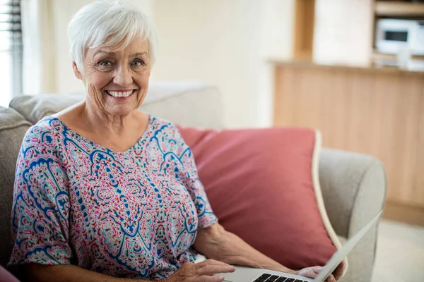 Portret van gelukkig senior vrouw met laptop in de woonkamer — Stockfoto