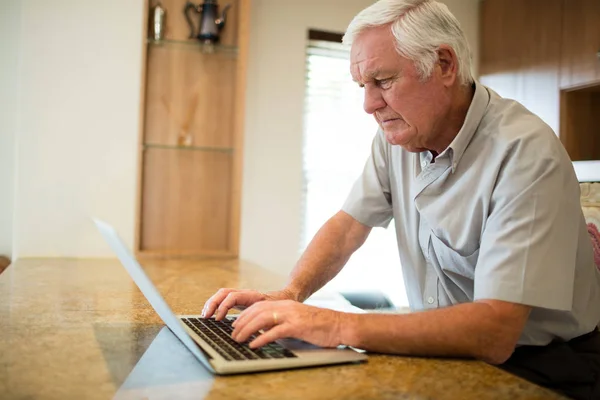 Uomo anziano utilizzando il computer portatile in cucina — Foto Stock