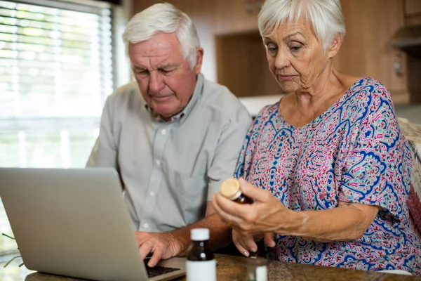 Senior paar laptop gebruikt en houden van pil fles in keuken — Stockfoto