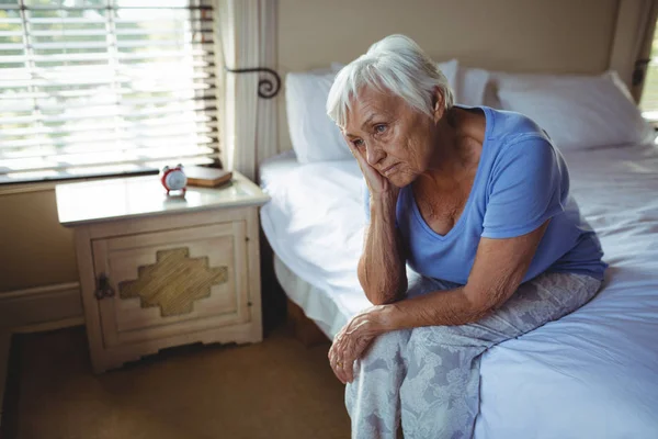 Besorgte Seniorin sitzt auf Bett im Schlafzimmer — Stockfoto