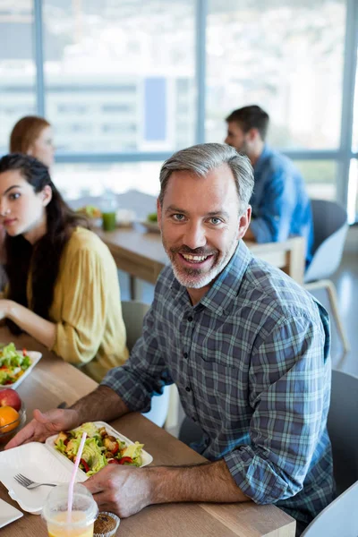 Hombre sonriente comiendo con sus colegas — Foto de Stock
