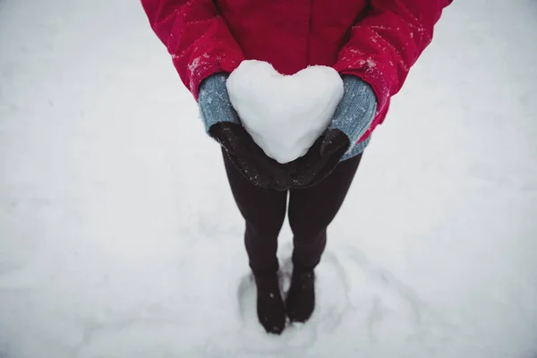 Kvinna i varma kläder håller snöiga hjärta — Stockfoto