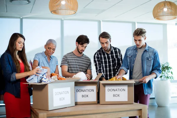 Equipo creativo del negocio que clasifica la ropa en la caja de la donación —  Fotos de Stock