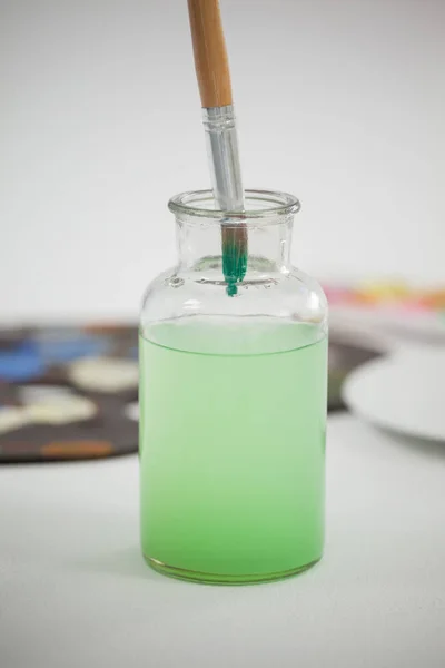 Paintbrush with green paint dipped into a jar filled with water — Stock Photo, Image