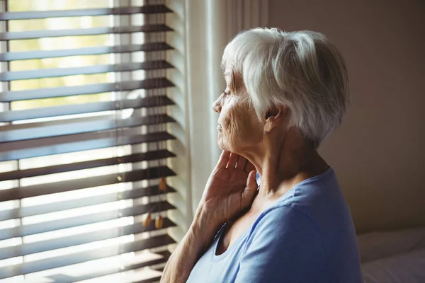 Задумчивая пожилая женщина смотрит из окна — стоковое фото