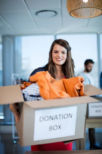Mujer sonriente sosteniendo una caja de donación en la oficina — Foto de Stock