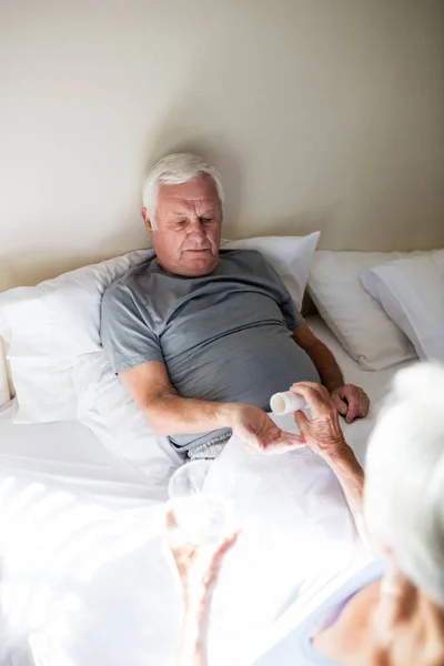 Mujer mayor dando medicina a hombre mayor en el dormitorio — Foto de Stock