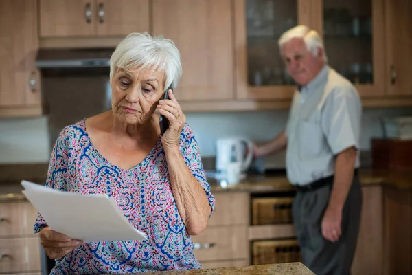 Senior woman talking on phone while man working in kitchen — Stock Photo, Image