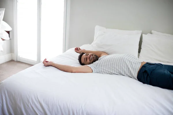 Uomo sdraiato sul letto con le braccia alzate sul letto — Foto Stock