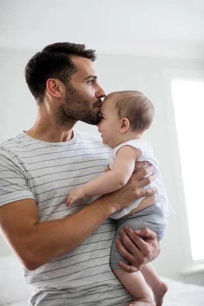 Father holding kissing his baby girl on forehead — Stock Photo, Image